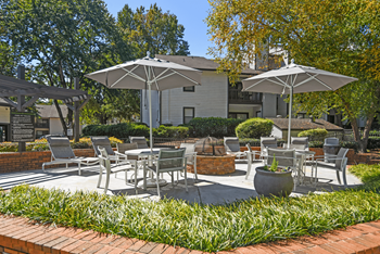 A patio with chairs and umbrellas is surrounded by green plants.